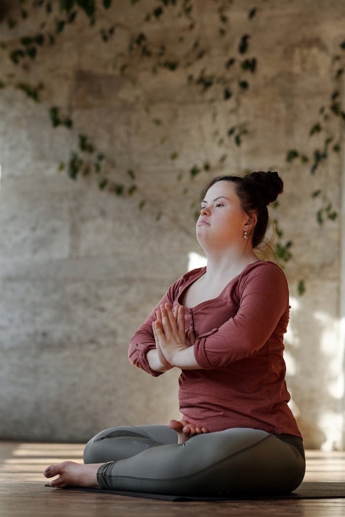 services-03 A young woman with Down syndrome focuses on inner peace while practicing yoga indoors.