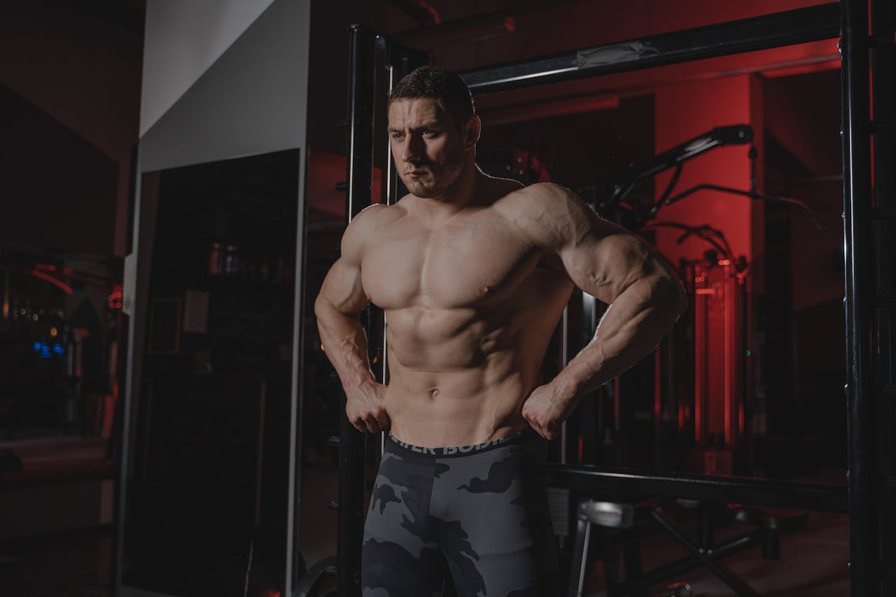 Shirtless bodybuilder flexing muscles under dramatic gym lighting. Fitness and strength.